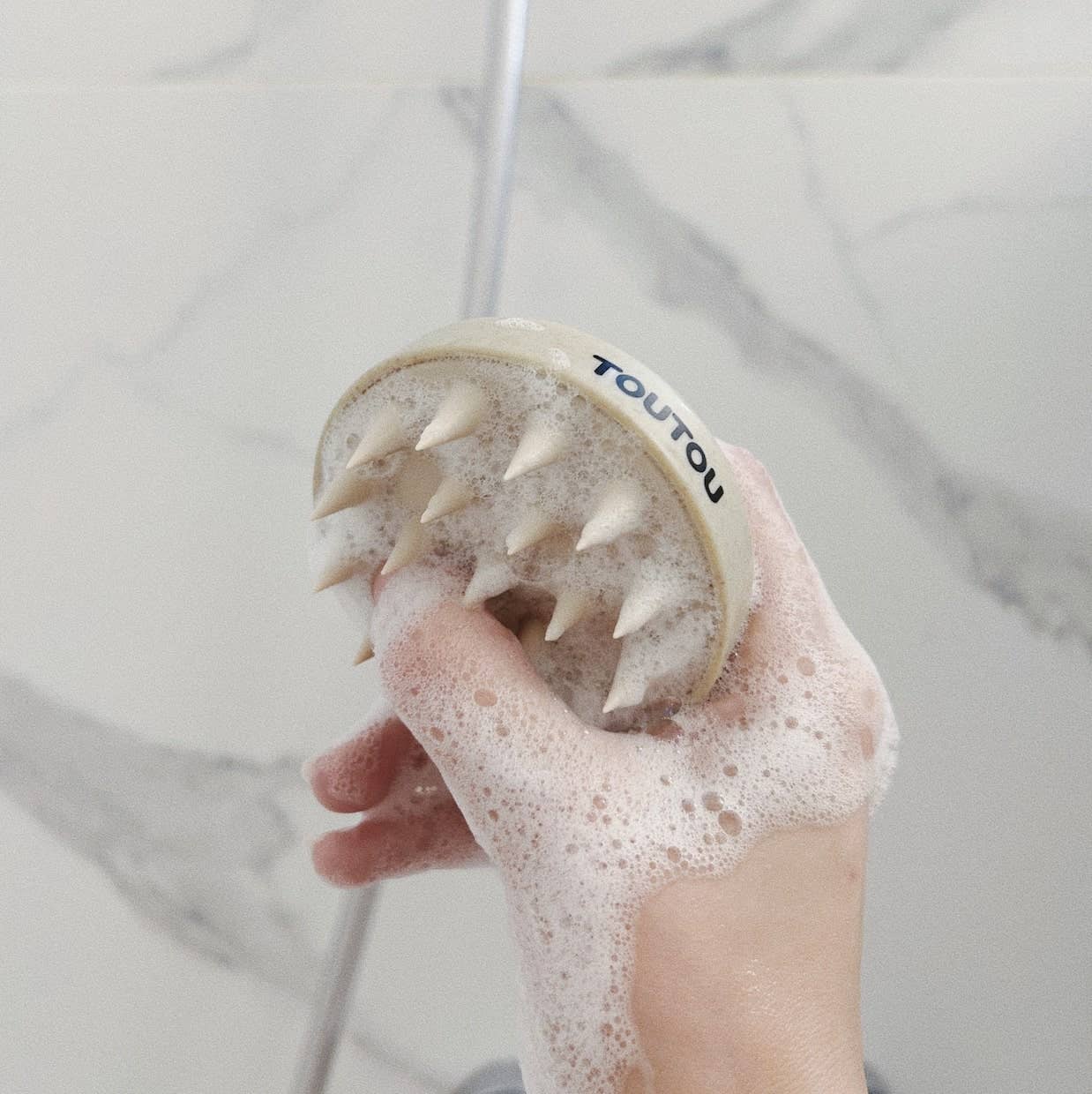 Hand using a scrubber with foam on a blurred bathroom background