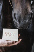 A close-up of a horse's nose and mouth area reaching toward a hand holding a rectangular cream-colored soap bar embossed with the text 'FRENKY LEWIS'.