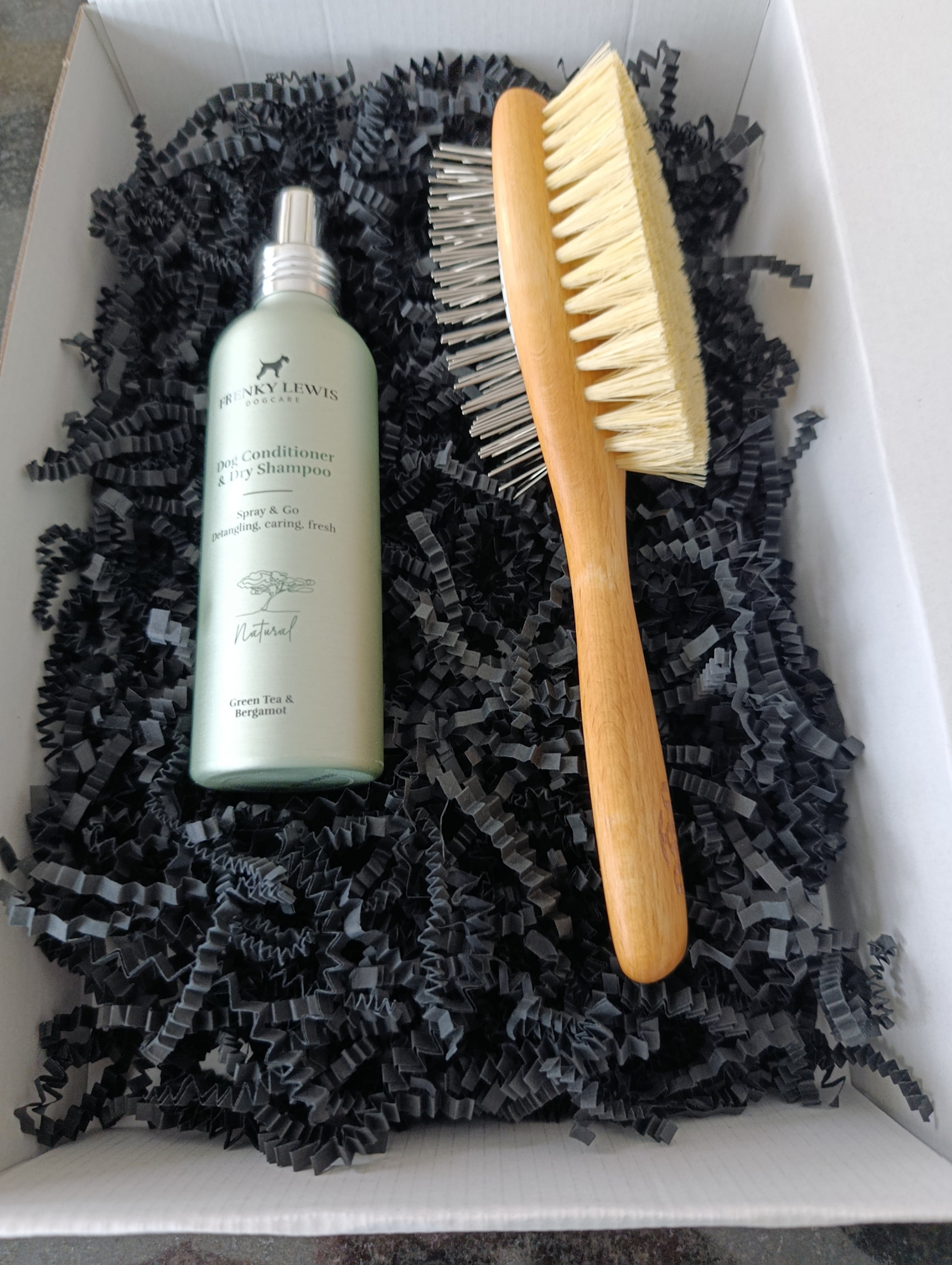 Bottle of shampoo and a brush on black textured material inside a box